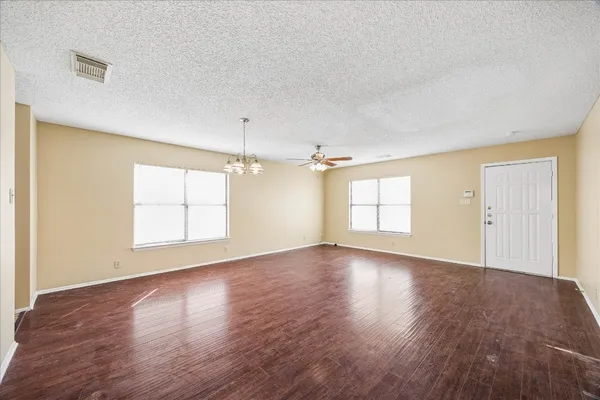 an empty room with wooden floor ceiling fan and windows