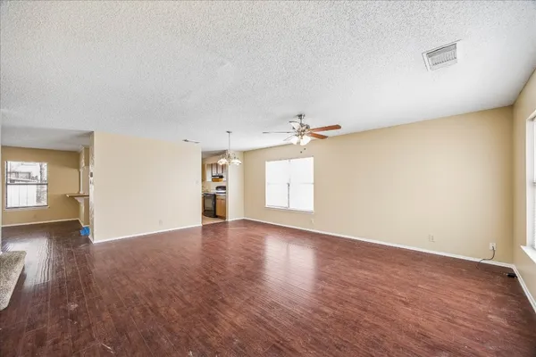 an empty room with wooden floor chandelier fan and windows