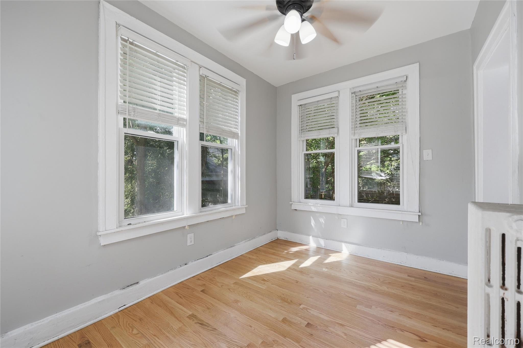 1945 Atkinson Street Detroit, MI 48206 - Photo 17 of 49 Room with light wood-finish flooring, two large windows with blinds, a ceiling fan with integrated lighting, and a white wall-mounted radiator
