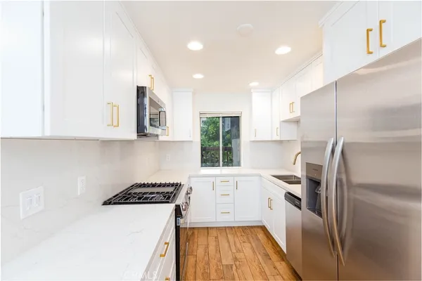 a kitchen with stainless steel appliances granite countertop a refrigerator a sink dishwasher a stove and white countertops with wooden floor