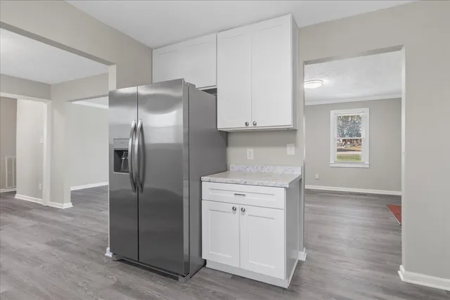 a kitchen with stainless steel appliances granite countertop a refrigerator a sink and white cabinets with wooden floors