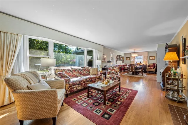a view of a dining room and livingroom with furniture wooden floor a rug a painting and a chandelier