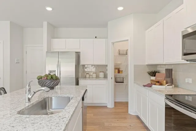 a kitchen with stainless steel appliances granite countertop a refrigerator a sink and white cabinets