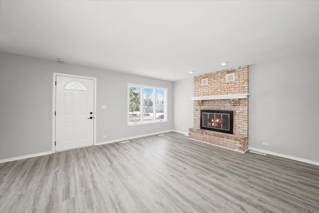 an empty room with wooden floor fireplace and windows