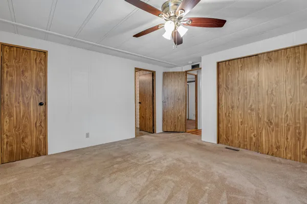 an empty room with a chandelier fan and closet area