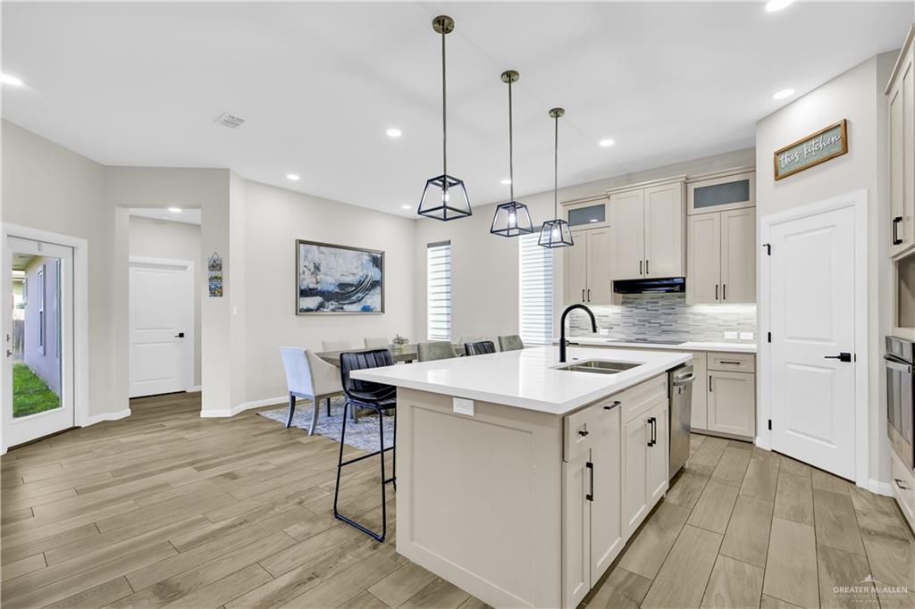 2514 Yarrow Street Mission, TX 78574 - Photo 4 of 22 Kitchen featuring an island with sink, a breakfast bar area, hanging light fixtures, light wood-style floors, and glass fronted cabinets