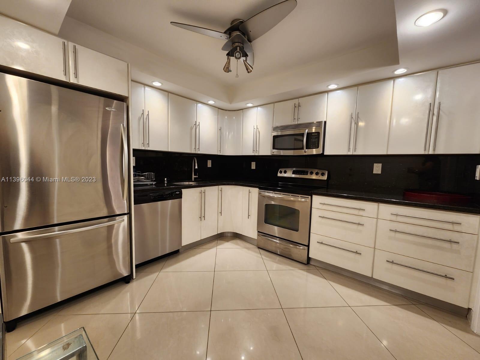 a kitchen with granite countertop a refrigerator a sink and white cabinets