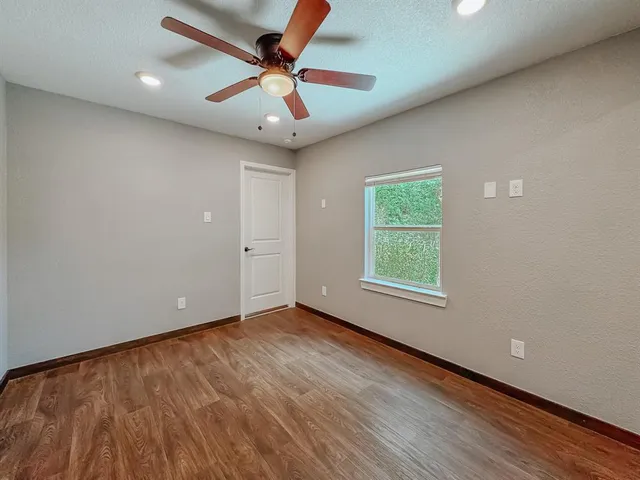 an empty room with wooden floor ceiling fan and windows