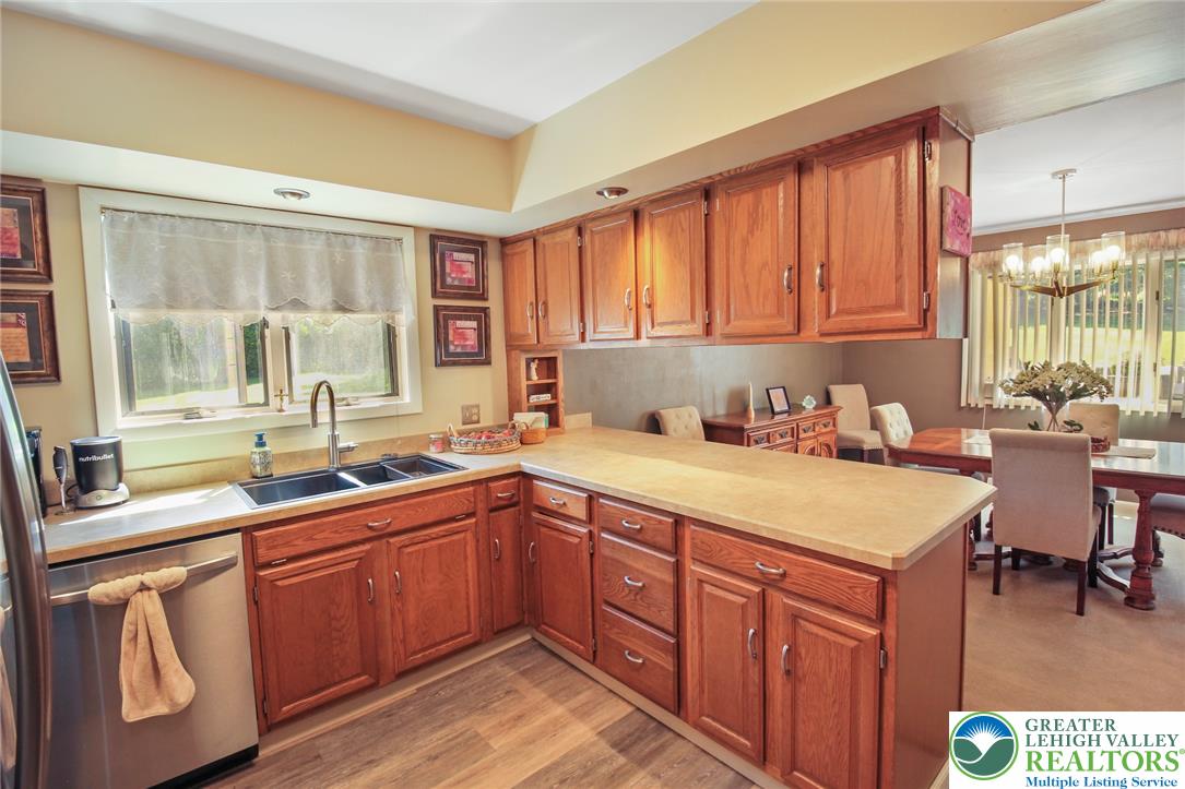 3470 Brodhead Road Bethlehem, PA 18020 - Photo 48 of 84 A functional kitchen provides ample wood cabinetry and counter space, with a double basin sink beneath a sunlit window, opening to a dining area.