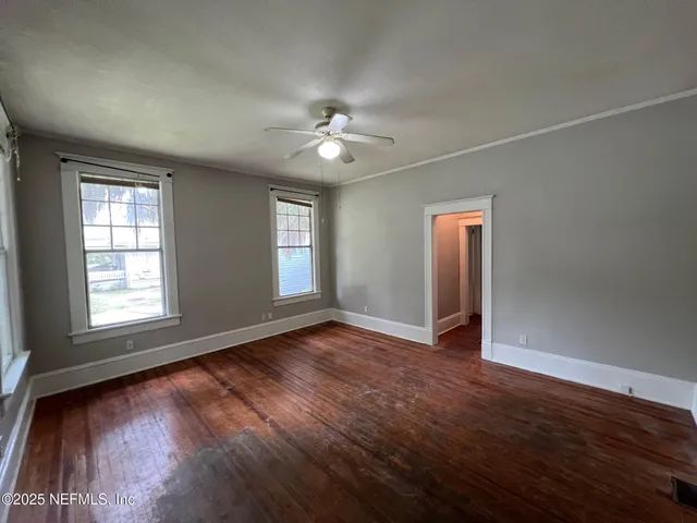 an empty room with wooden floor chandelier fan and windows