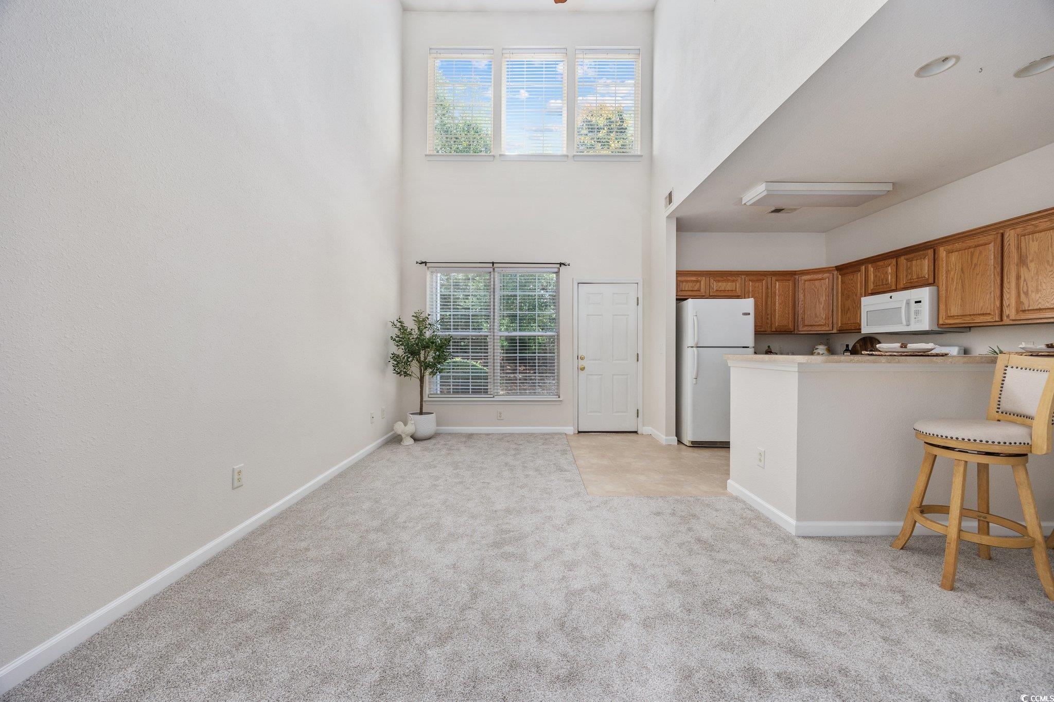 155 Chenoa Drive, Unit E Murrells Inlet, SC 29576 - Photo 4 of 34 Kitchen with white appliances, light carpet, healthy amount of natural light, brown cabinetry, and a high ceiling