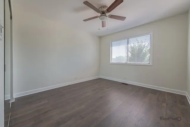 an empty room with wooden floor ceiling fan and windows