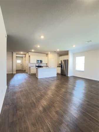 a view of empty room with wooden floor and kitchen