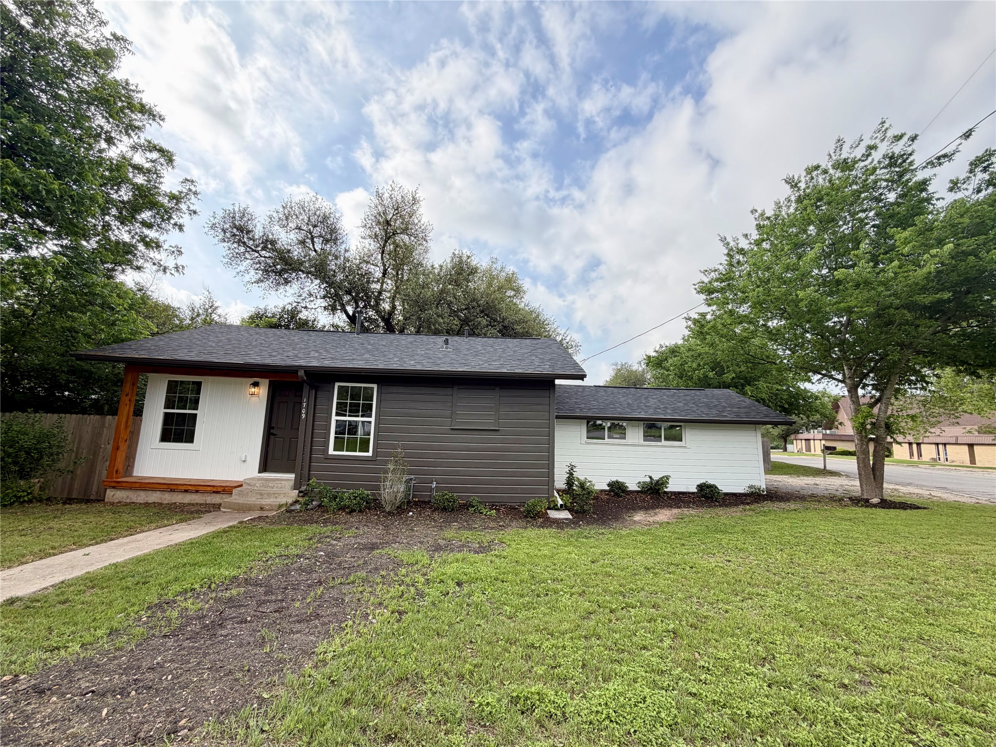 1709 Cecelia Street Taylor, TX 76574 - Photo 4 of 37 Exterior featuring modern two-tone siding, a covered entry porch with wood-finish columns, a dark shingle roof, and a concrete pathway
