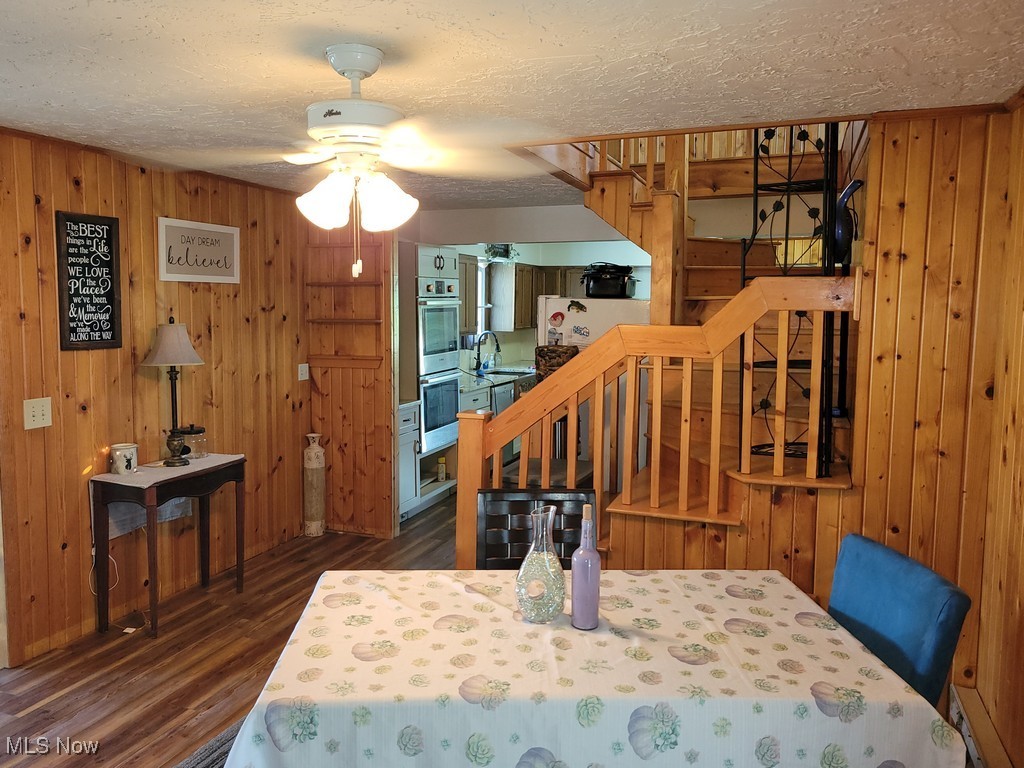 42774 Webster Road Lagrange, OH 44050 - Photo 12 of 37 Dining space with wood walls, stairs, a textured ceiling, dark wood-type flooring, and a ceiling fan