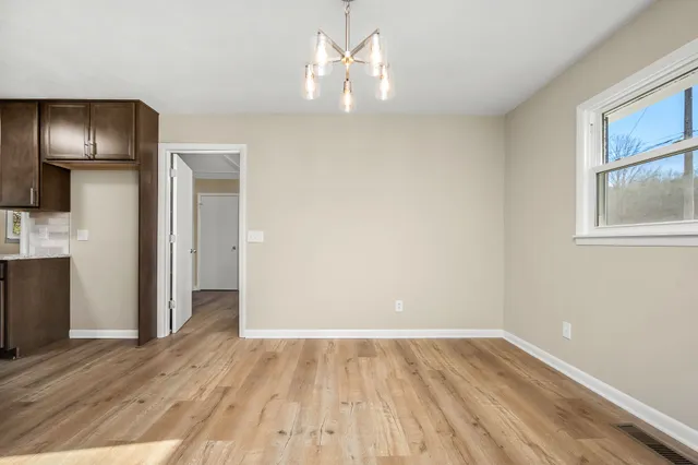 a view of empty room with wooden floor and kitchen