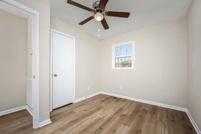 an empty room with wooden floor ceiling fan and windows