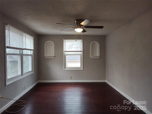 an empty room with wooden floor chandelier fan and windows