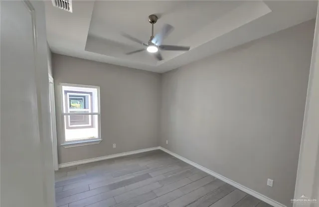 an empty room with wooden floor chandelier fan and windows