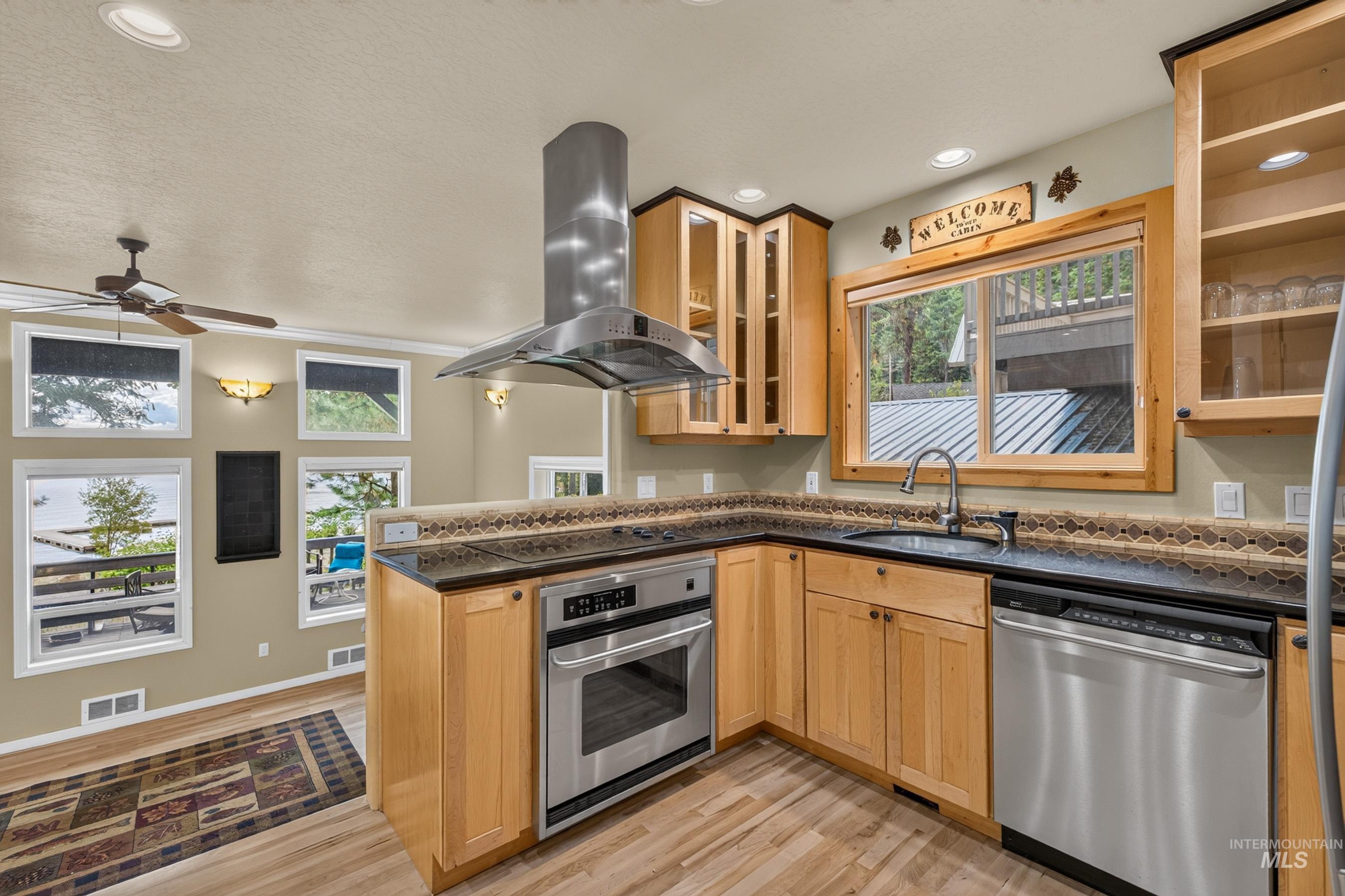 3531 Kp Cove Road McCall, ID 83638 - Photo 13 of 49 Hardwood flooring, stone fireplace with a wood-burning stove, built-in kitchen cabinetry with glass doors, recessed lighting, and a ceiling fan