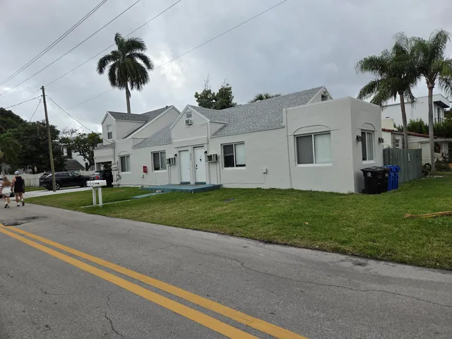 a view of a white house with a yard plants and palm trees