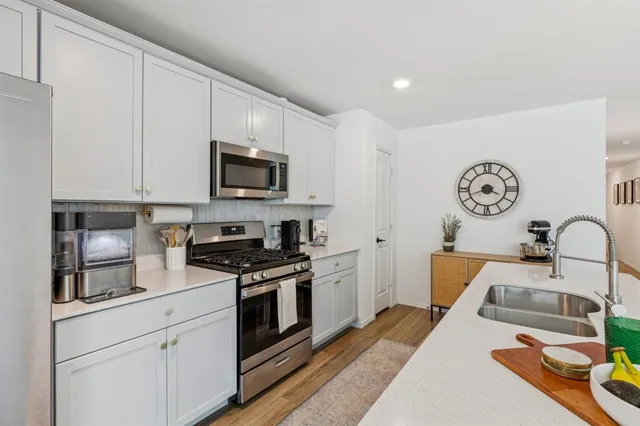 a kitchen with stainless steel appliances granite countertop a stove top oven a sink dishwasher and white cabinets with wooden floor