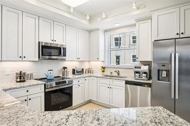a kitchen with stainless steel appliances granite countertop a refrigerator stove a sink and white cabinets