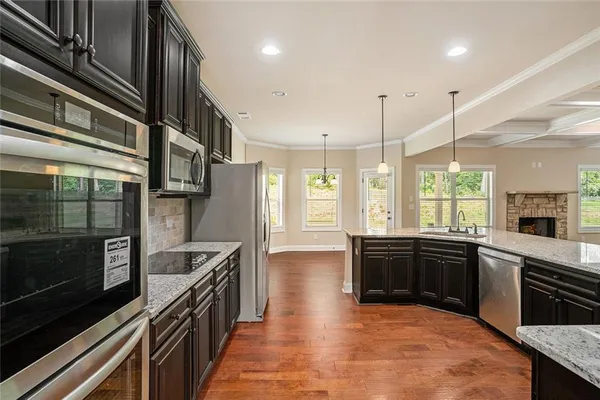 a large kitchen with stainless steel appliances granite countertop a stove a sink dishwasher a microwave oven and a refrigerator with wooden floor