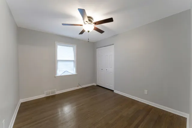 an empty room with wooden floor fan and windows