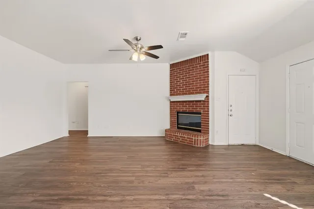 a view of an empty room with wooden floor and a ceiling fan