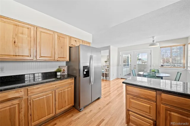 a kitchen with granite countertop a refrigerator a sink dishwasher stove and white cabinets with wooden floor