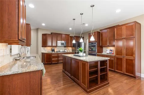 a open kitchen with stainless steel appliances granite countertop a stove top oven a sink dishwasher a dining table and chairs with wooden floor