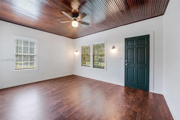 an empty room with wooden floor chandelier fan and windows