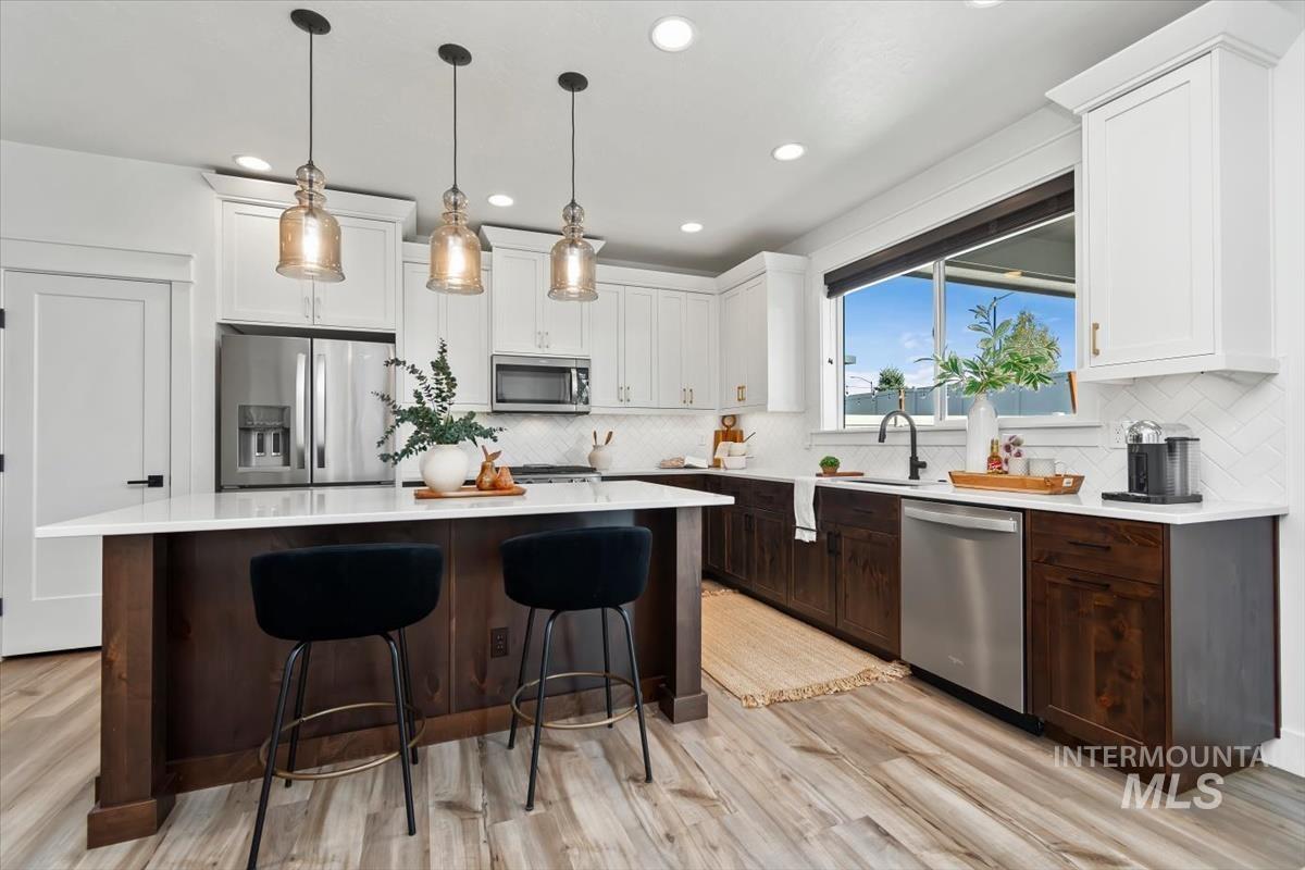 5897 West Riva Capri Street Meridian, ID 83646 - Photo 1 of 50 Modern kitchen featuring a two-toned cabinetry scheme, a central island with countertop seating, stainless steel appliances, pendant lighting, and a window above the sink