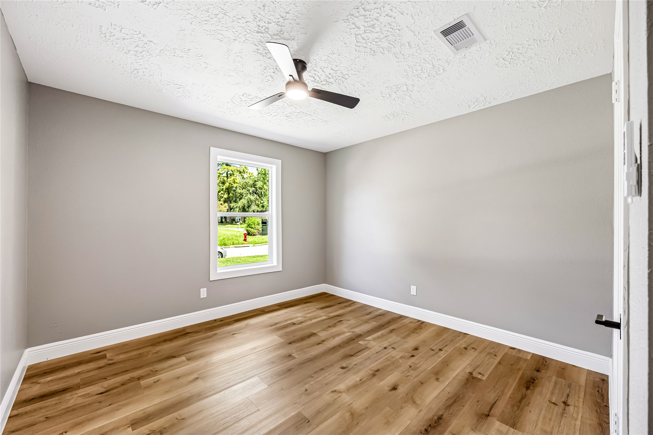 4534 Rosegate Drive Spring, TX 77373 - Photo 17 of 24 Bright and comfortable bedroom featuring warm wood-look flooring, soft neutral walls, a modern ceiling fan, and crisp white trim. A large window brings in natural light, creating a fresh and inviting space ready to personalize.