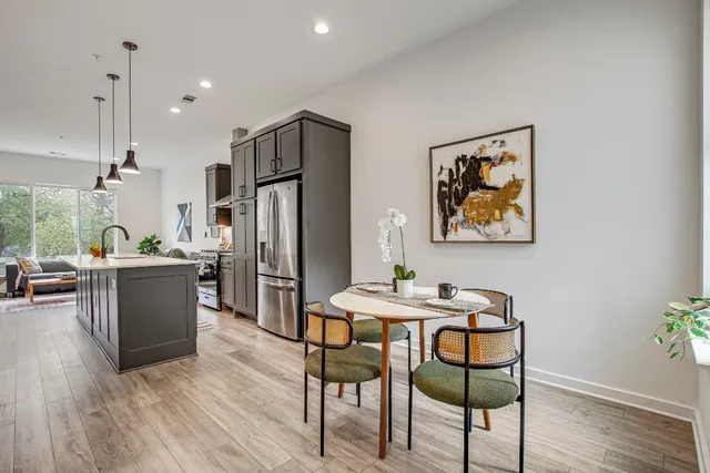 a kitchen with stainless steel appliances kitchen island granite countertop a refrigerator a stove a dining table and chairs with wooden floor