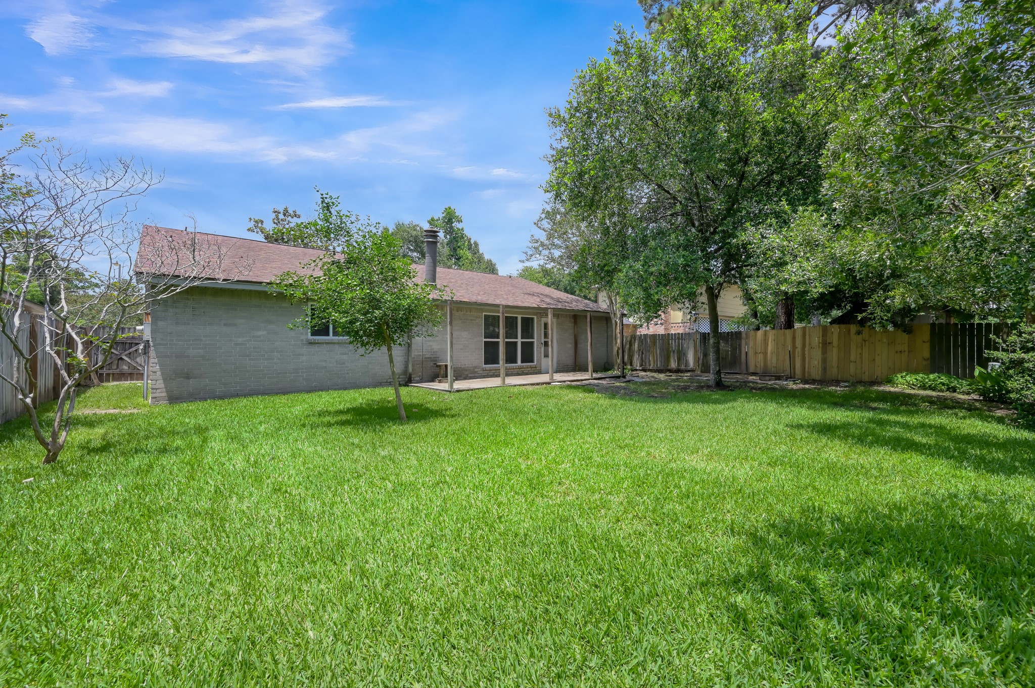 4314 Enchantedgate Drive Spring, TX 77373 - Photo 39 of 47 Generous backyard with a well-maintained lawn, mature trees providing shade, and a wooden fence for privacy. The house features a patio area, ideal for outdoor activities and relaxation.