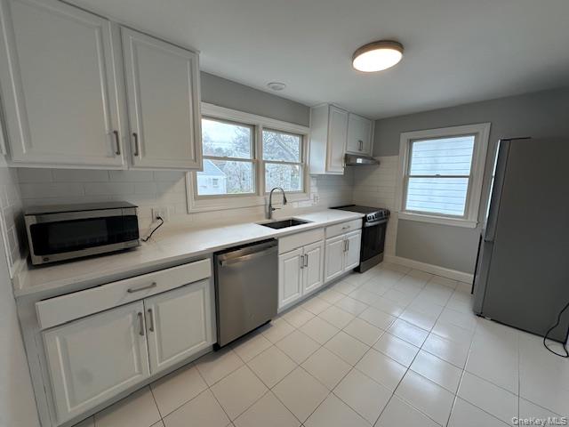 7 Linwood Road North, Unit 2 Port Washington, NY 11050 - Photo 2 of 13 Kitchen featuring white cabinetry, stainless steel appliances, backsplash, light countertops, and light tile patterned flooring