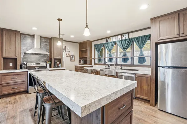 a kitchen with kitchen island a stove a refrigerator a oven and a sink with wooden floor