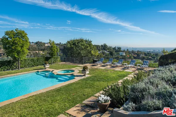 a view of a swimming pool with lawn chairs plants and large trees