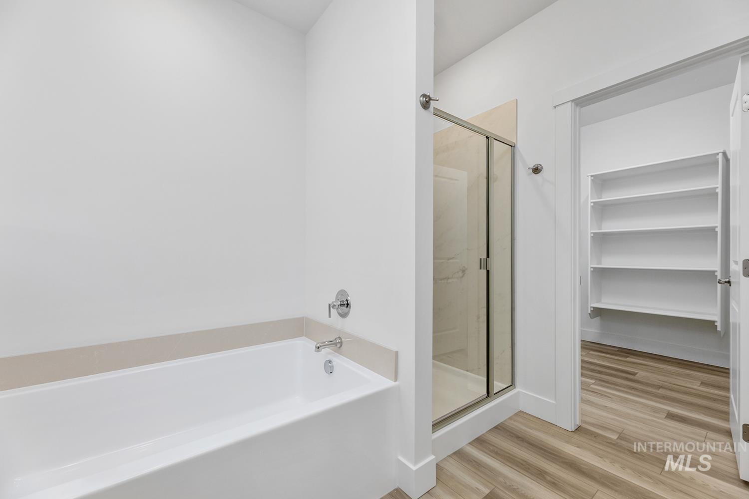 4548 West Wapoot Street Meridian, ID 83646 - Photo 15 of 17 Bathroom featuring a white soaking tub with chrome fixtures, a glass-enclosed shower, wood-finish flooring, and an open doorway revealing built-in shelving