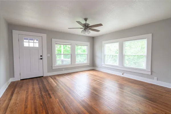 an empty room with wooden floor windows and fan