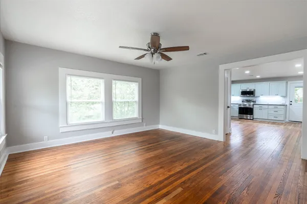 an empty room with wooden floor windows and a ceiling fan