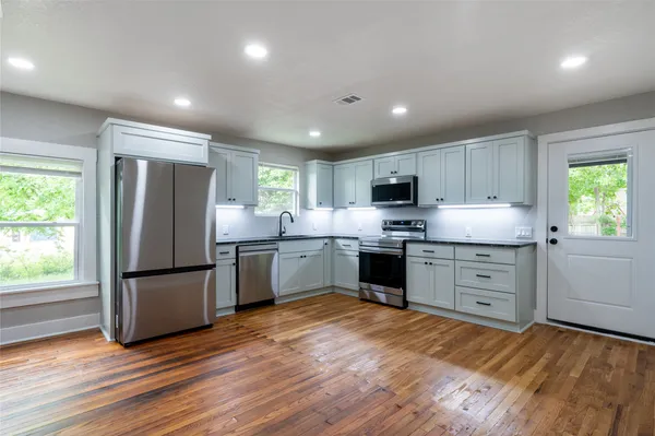 a kitchen with granite countertop a refrigerator oven a sink dishwasher and a stove with wooden floor