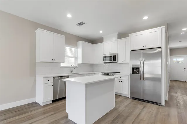 a kitchen with stainless steel appliances granite countertop a refrigerator a sink a stove and white cabinets with wooden floor