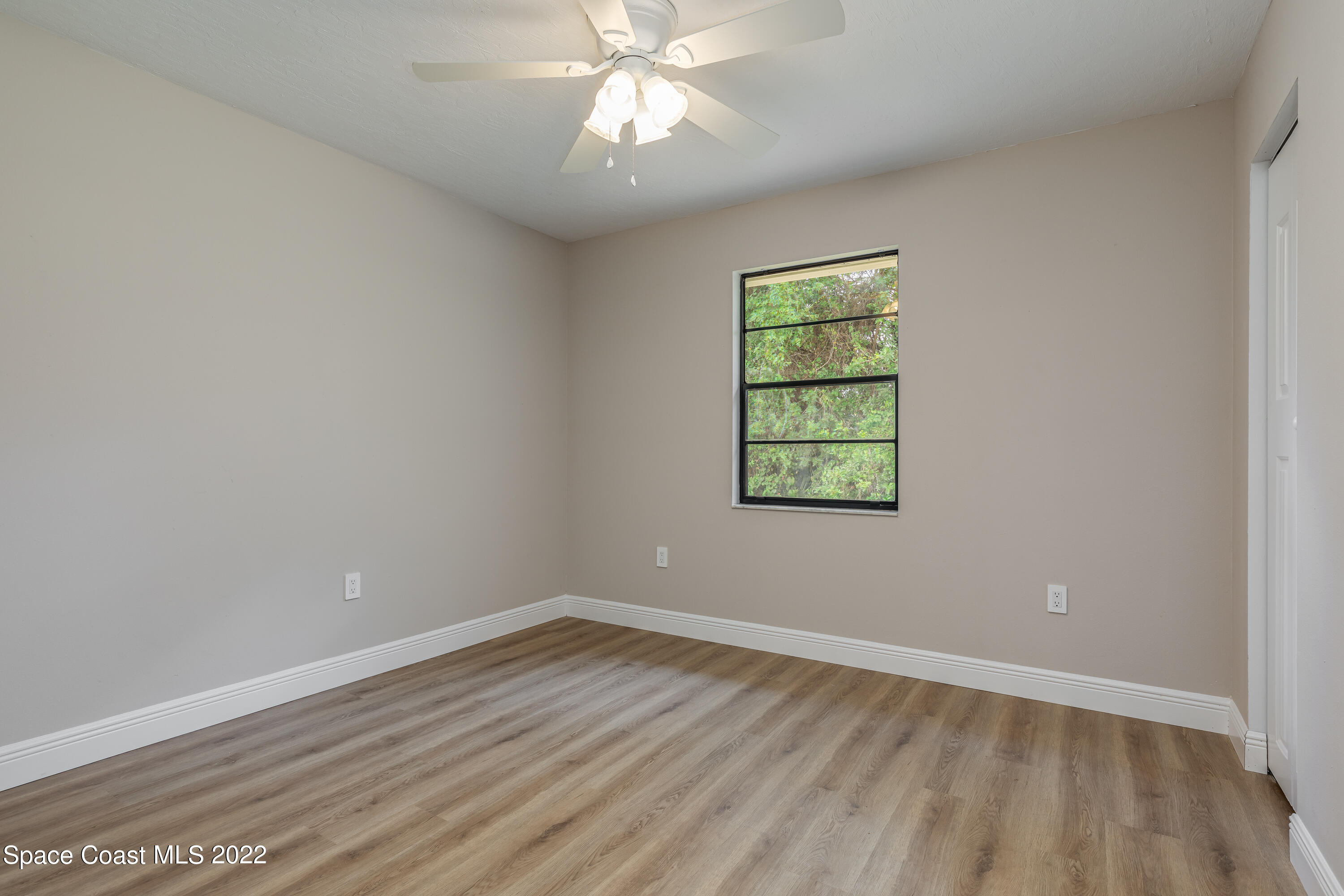1011 Thompson Road Southwest Palm Bay, FL 32908 - Photo 16 of 17 an empty room with wooden floor chandelier fan and windows
