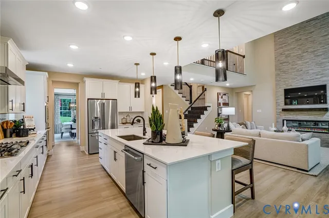 a kitchen with stainless steel appliances kitchen island a refrigerator a stove a sink dishwasher a dining table and chairs with wooden floor