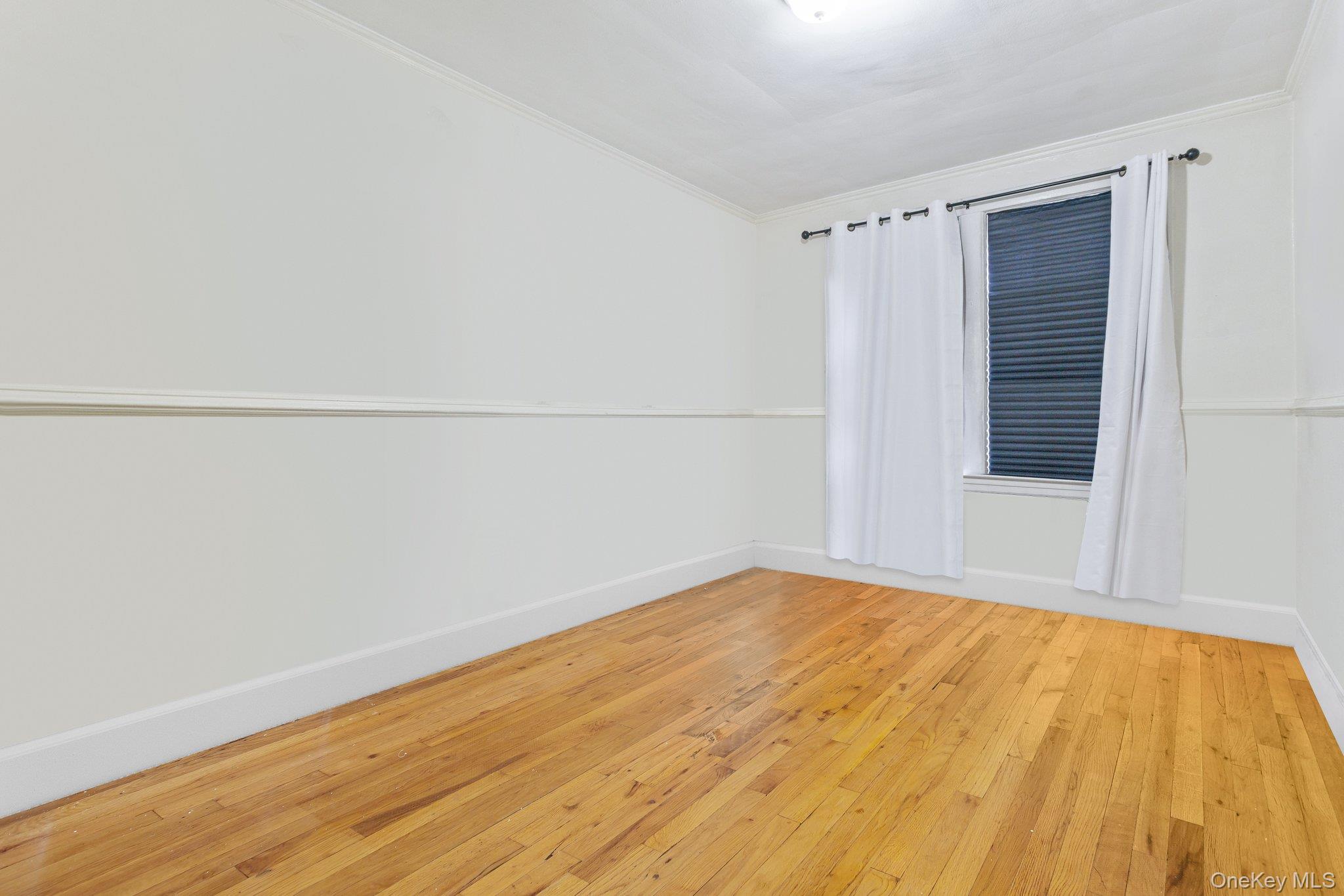 34-29 58th Street Queens, NY 11377 - Photo 16 of 23 a view of an empty room with wooden floor and a window