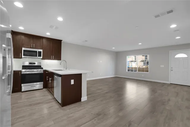 a large kitchen with stainless steel appliances a large counter top a sink dishwasher and a refrigerator with wooden floor