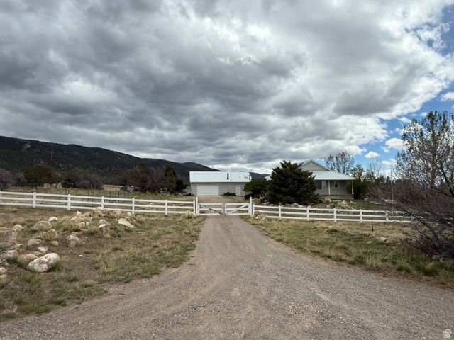 10000 North 6730th East Spring City, UT 84662 - Photo 3 of 31 Gravel driveway leading to a fenced property with a single-story residence and detached garage, featuring a white picket fence, covered front porch, and metal roofing
